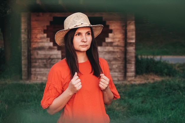 Linda mulher com um chapéu de palha vestido com roupas vermelhas fica no fundo de uma casa de madeira