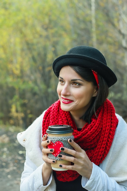 Linda mulher com um chapéu preto tem uma xícara aconchegante nas mãos. Sorriso alegre e bom humor