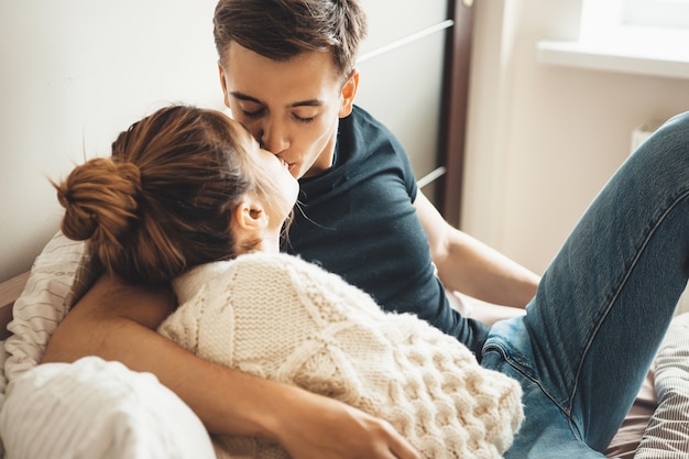 Linda mulher com um suéter de tricô branco beijando o marido enquanto estava deitada na cama