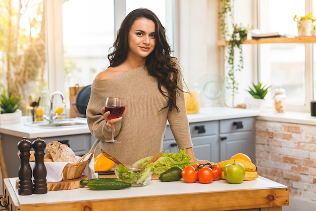 Linda mulher cozinhando e bebendo vinho em casa na cozinha.