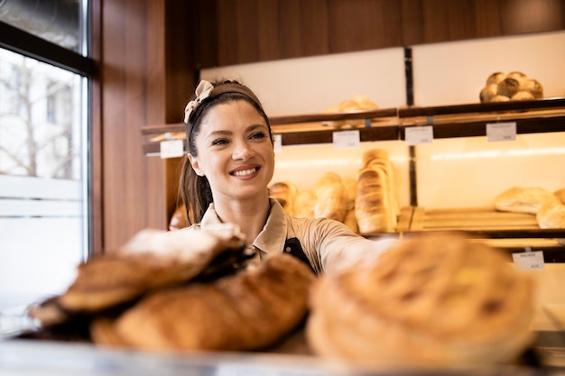 Linda mulher de avental vendendo massa e pão recém-assados na padaria