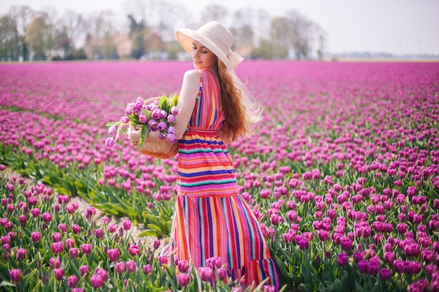 Linda mulher de cabelo vermelho, vestido listrado e segurando o buquê de flores tulipas na cesta