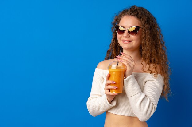 Linda mulher de cabelos cacheados bebendo suco de laranja contra um fundo azul