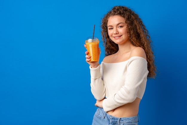 Linda mulher de cabelos cacheados bebendo suco de laranja contra um fundo azul