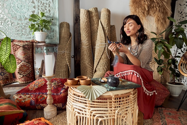 Linda mulher de cabelos escuros com roupa étnica xamânica em um quarto decorado em estilo bali fazendo cerimônia de rappa