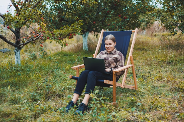 Linda mulher de camisa quadriculada com laptop trabalhando ao ar livre no conceito de escritório doméstico no jardim Trabalho remoto