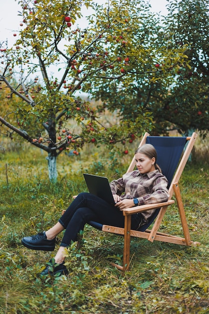 Linda mulher de camisa quadriculada com laptop trabalhando ao ar livre no conceito de escritório doméstico no jardim Trabalho remoto