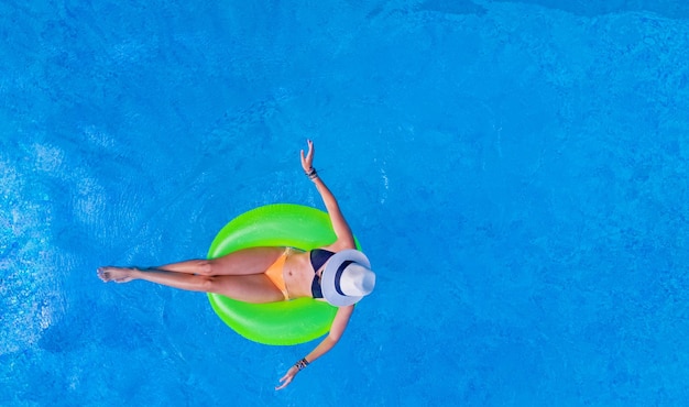 Linda mulher de chapéu na piscina vista aérea de cima de uma jovem de biquíni relaxa