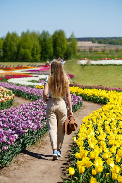 Linda mulher de chapéu rindo para a câmera no jardim de flores da primavera Menina com câmera sorrindo no parque com muitas flores Mulher aproveitando o tempo no campo de flores desabrochando Moça bonita andando no prado