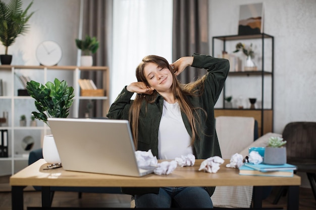 Linda mulher de escritório relaxando esticando seu corpo enquanto está sentada na frente de seu laptop