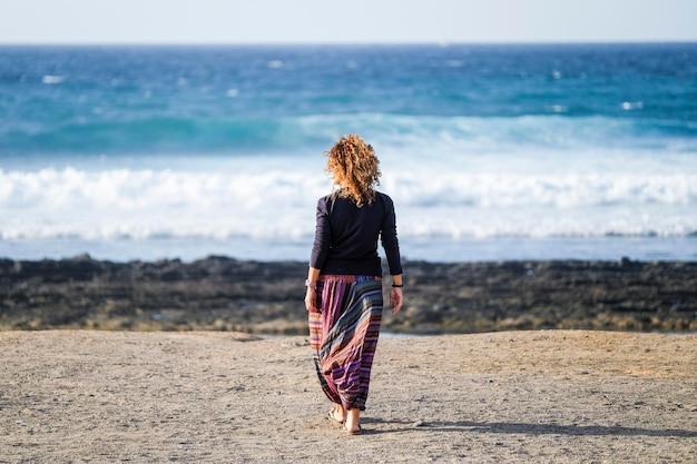 Linda mulher de meia idade caucasiana solitária anda e aproveita a praia de ninguém na liberdade da temporada e o conceito de estilo de vida alternativo para a senhora da independência sentindo o oceano e a natureza