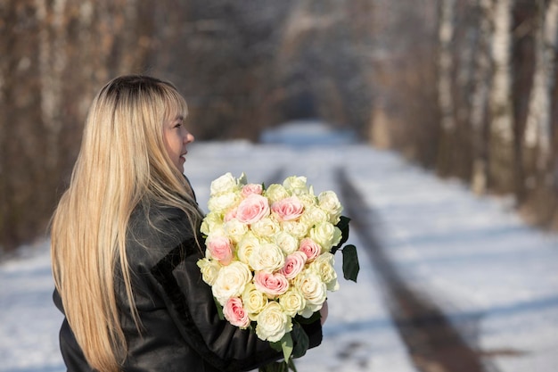 Linda mulher de meia idade com um buquê de rosas brancas na floresta de inverno