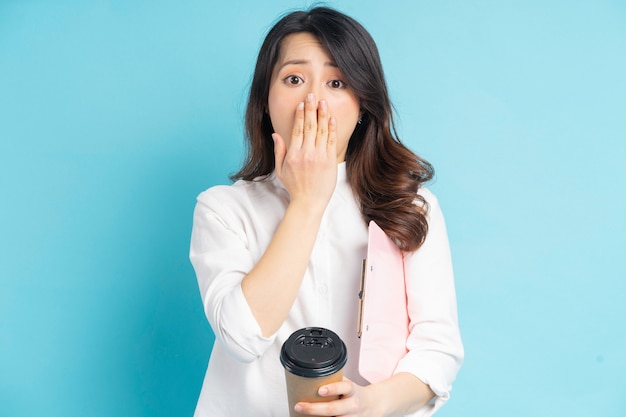 Linda mulher de negócios asiática segurando uma xícara de café de papel na mão, ela cerrou a boca com a mão em surpresa