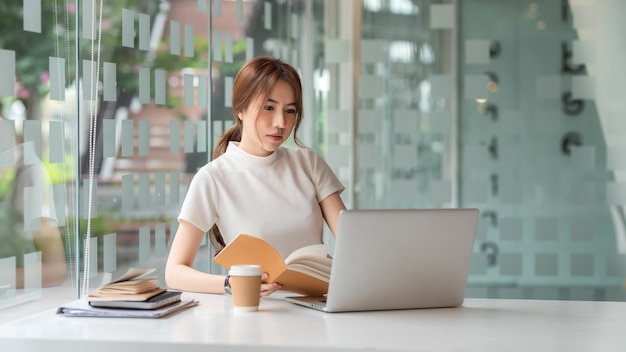 Linda mulher de negócios asiática sentada no escritório com um laptop e notebook.