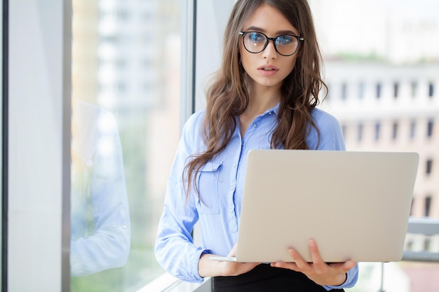 Linda mulher de negócios está usando um laptop e sorrindo enquanto trabalha no escritório