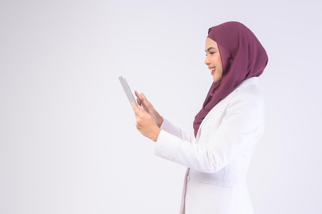 Linda mulher de negócios muçulmana vestindo terno branco com hijab segurando tablet em studiox9
