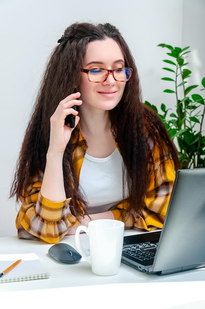 Linda mulher de óculos falando ao telefone no local de trabalho mulher trabalhando em casa