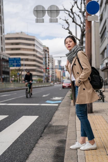 linda mulher de pé e esperando para atravessar a estrada. ela está usando um lenço cinza