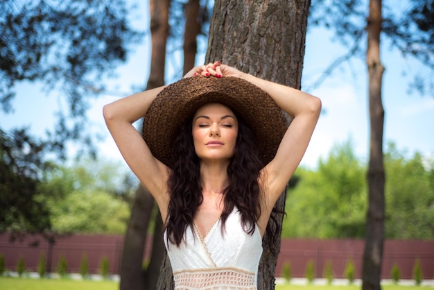 Linda mulher de vestido branco de verão e chapéu de palha no jardim