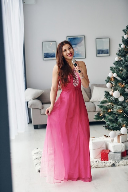 Linda mulher de vestido rosa cantando dentro de casa na festa de ano novo
