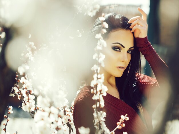 Linda mulher de vestido vermelho perto da árvore de damasco com flores desabrochando