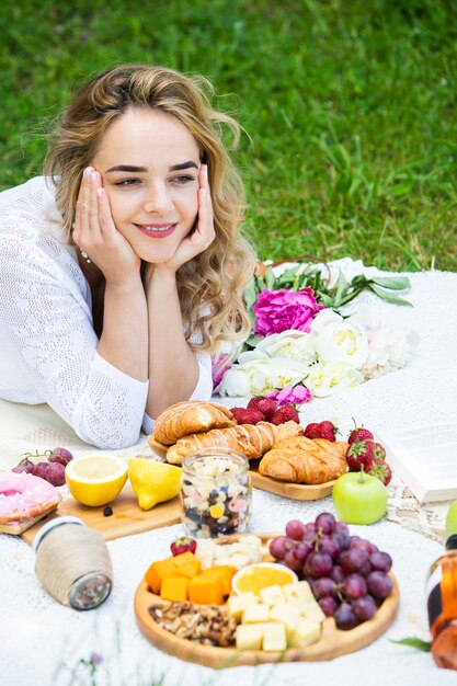 Linda mulher descansando em um parque sentada em uma toalha de piquenique com frutas e vinho