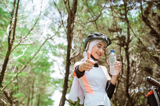 Linda mulher desportiva em hijab segurando garrafa com polegares para cima