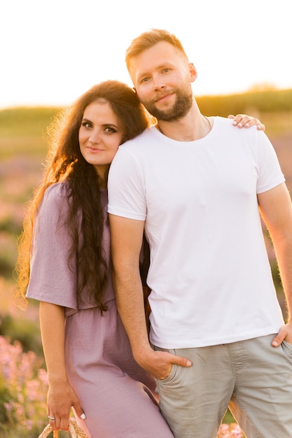 Linda mulher elegante com cesta de piquenique pegando a mão de um homem encantador andando na lavanda