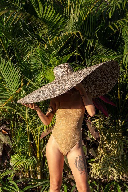 Linda mulher elegante e atraente em traje de banho e chapéu de palha por natureza tropical