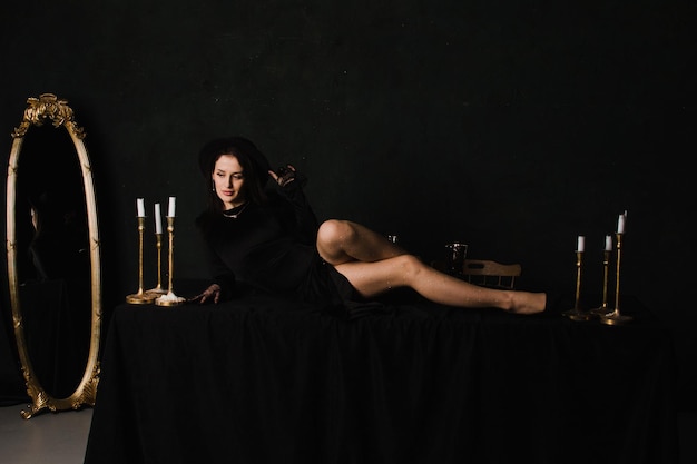 Linda mulher elegante em luvas e um vestido se senta em uma mesa em um fundo preto