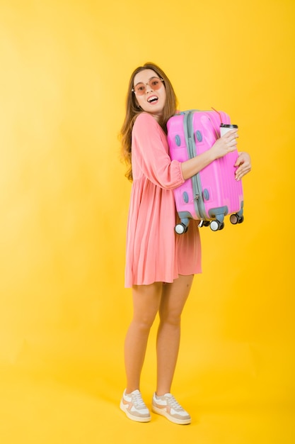 Linda mulher elegante em um vestido rosa com uma mala grande rosa para viajar