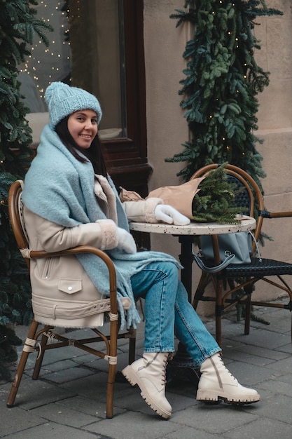 Linda mulher elegante sentada na cadeira no café ao ar livre com buquê de árvore de natal