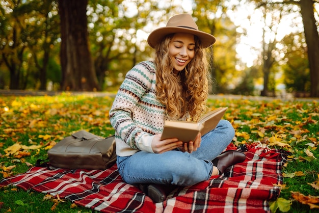 Linda mulher encaracolada de chapéu na esteira com livro no parque outono Solitude de relaxamento com a natureza