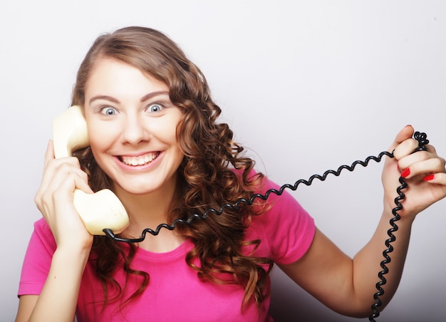 Foto linda mulher encaracolada espantada falando em um telefone vintage branco isolado sobre um fundo branco