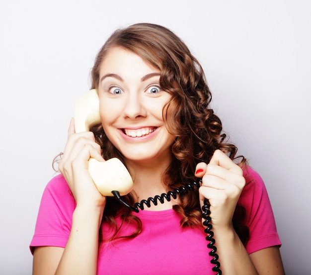 Linda mulher encaracolada espantada falando em um telefone vintage branco isolado sobre um fundo branco