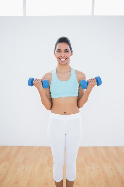 Linda mulher esbelta levantando dumbbells azuis