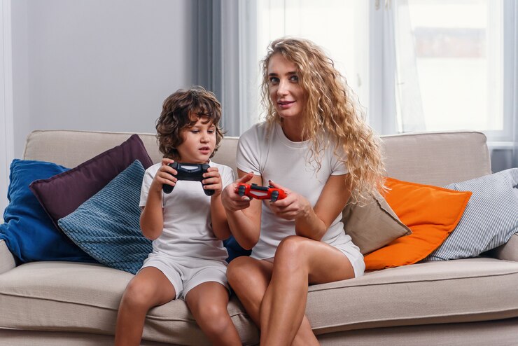 Linda mulher esbelta loira que jogando videogame interessante com gamepad junto com seu belo filho sorridente, sentado no sofá aconchegante em casa.