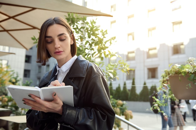 Linda mulher escrevendo textos no bloco de notas, sentada ao ar livre na esplanada de um parque público