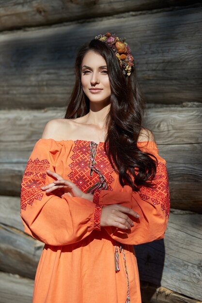 Linda mulher eslava com um vestido étnico laranja e uma coroa de flores na cabeça