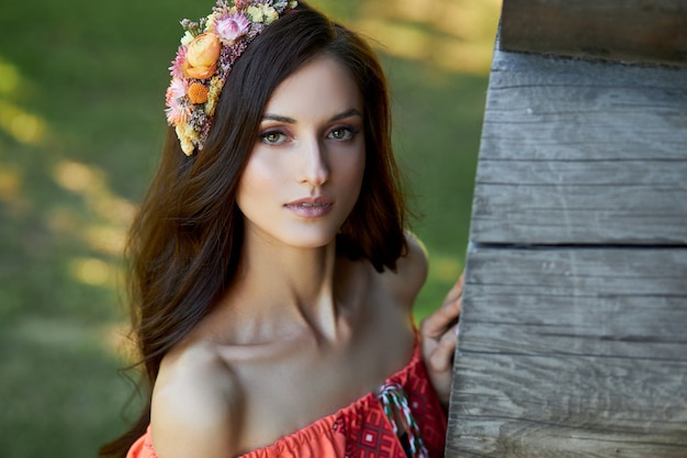 Linda mulher eslava em um vestido laranja étnico e uma coroa de flores na cabeça. bela maquiagem natural. retrato de uma garota russa