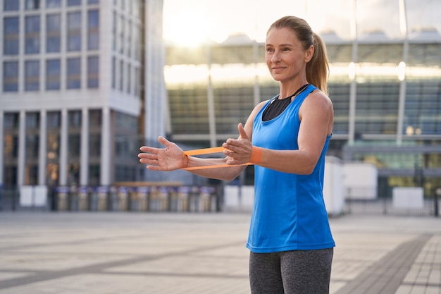 Linda mulher esportiva em roupas esportivas femininas, segurando a faixa de resistência em pé