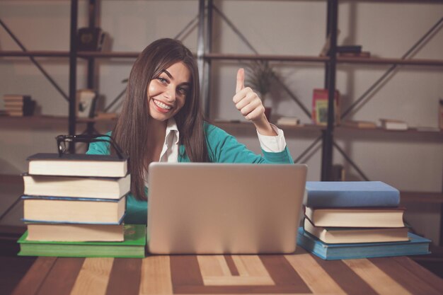 Foto linda mulher está feliz com seu trabalho bem sucedido com laptop na mesa de madeira