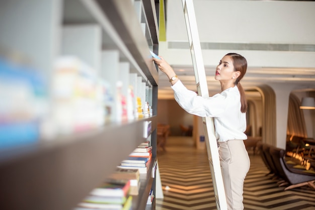 Linda mulher está lendo livros na biblioteca