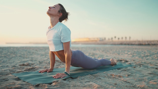 Foto linda mulher esticando o exercício no tapete de ioga ao ar livre garota esportiva praticando ioga para ficar em forma yoga na praia