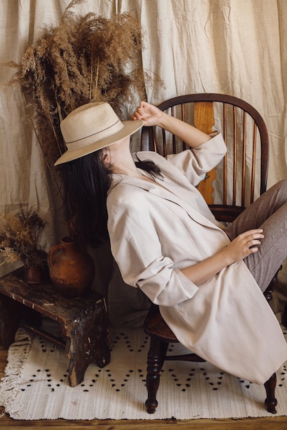 Foto linda mulher estilosa de terno sentada em uma cadeira de madeira retrô em uma sala de estilo boêmio com grama seca