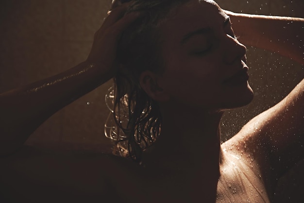 Linda mulher europeia satisfeita lava xampu do cabelo da cabeça no banheiro, toma banho e gosta, sorrindo