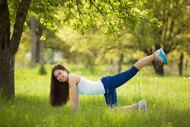 Linda mulher exercitando ao ar livre. Alegre garota magro fazendo exercícios no parque no horário de verão