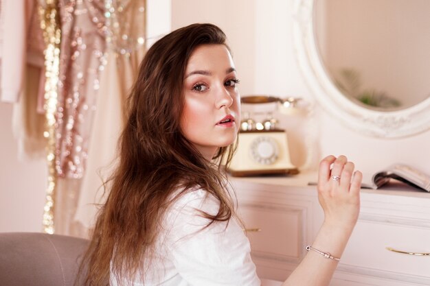 Linda mulher feliz em seu quarto perto de sua penteadeira, posando antes do camarim rosa de festa