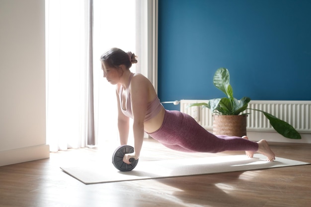 Linda mulher forte em roupas esportivas está malhando com roda de exercícios em casa na sala conceito de esporte e recreação roda de treinamento na sala de estar