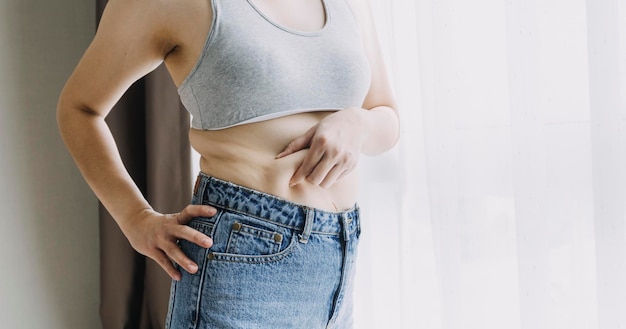 Linda mulher gorda com fita métrica Ela usa a mão para espremer o excesso de gordura que está isolado em um fundo branco Ela quer perder peso o conceito de cirurgia e quebrar a gordura sob o